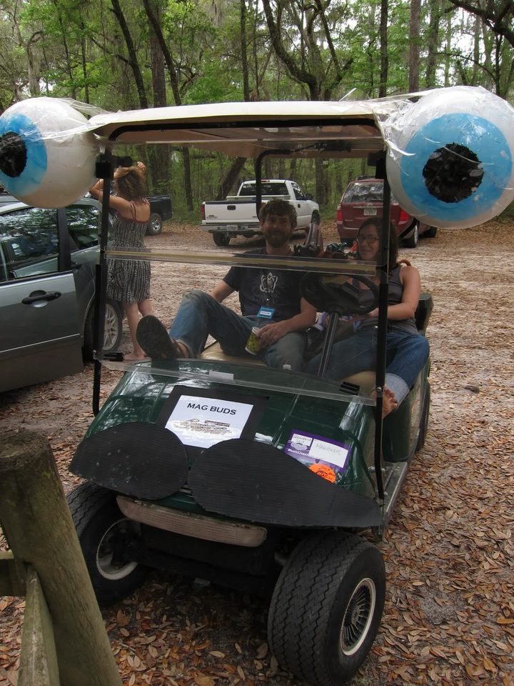 Two riders lounge in the original green Zerble at SpringFest 2011, feet up behind the windshield, under the giant blue eyeballs.