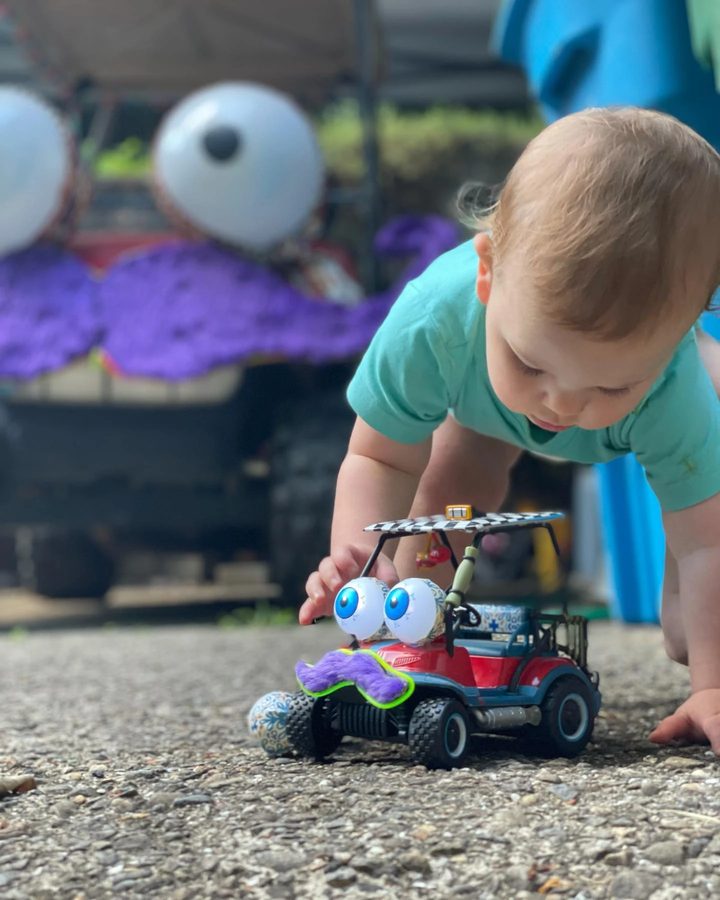 Darwin crawls toward the RC Zerble, a toy cart with googly eyes and a fuzzy purple mustache, with the real Zerble's giant eyes and purple mustache parked in the background.