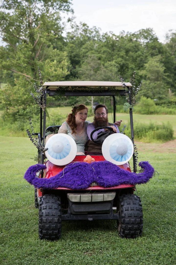 Gary and Fox ride Zerble on their wedding day: the red cart trimmed with eucalyptus and ferns, with its big eyes, orange nose, and fuzzy purple mustache.